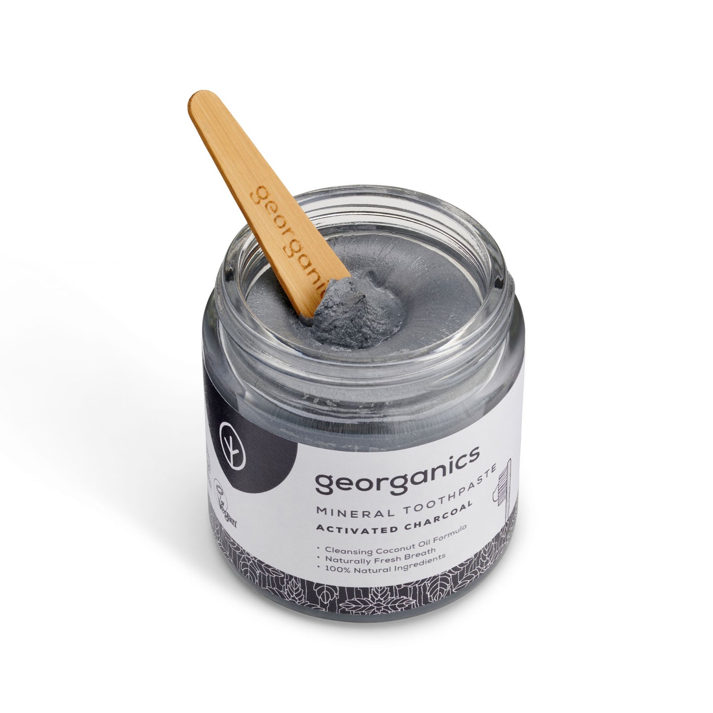Jar of georganics charcoal mineral toothpaste with a wooden spatula on a white background