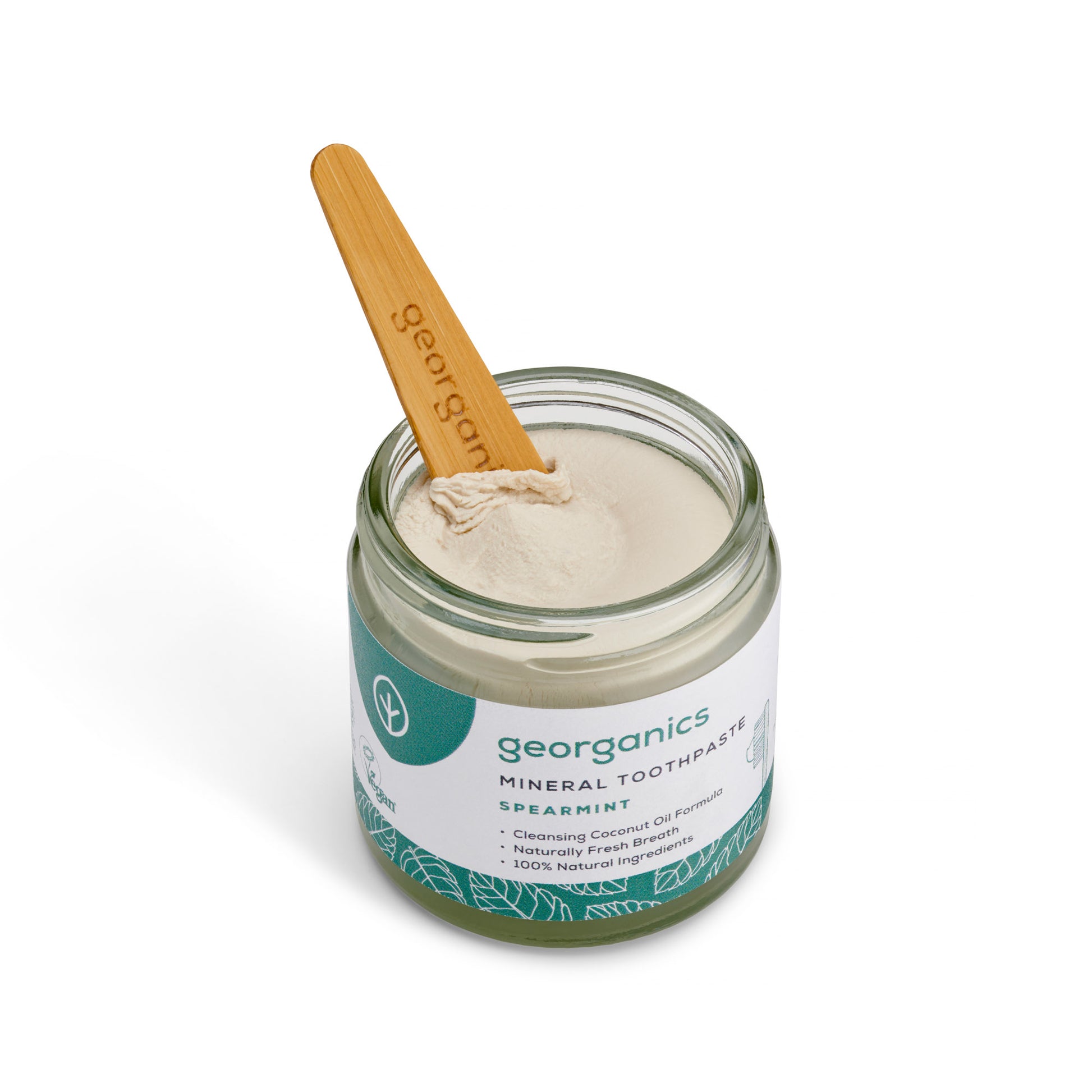 Jar of georganics spearmint mineral toothpaste with a wooden spoon on a white background