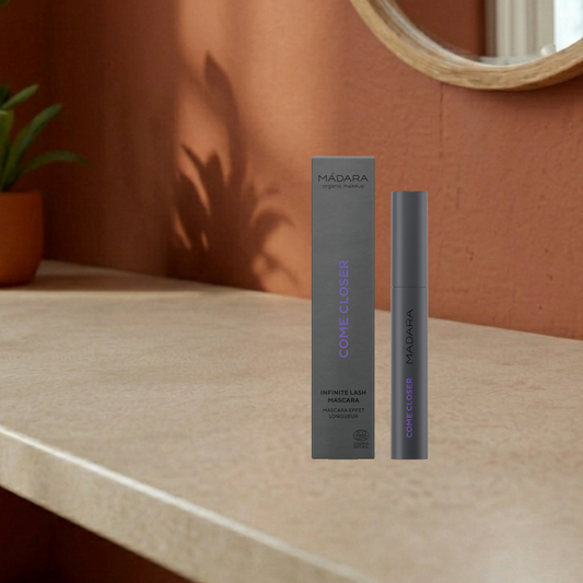 MADARA infinite mascara come closer with grey box and tube on a beige surface against a warm-toned wall.