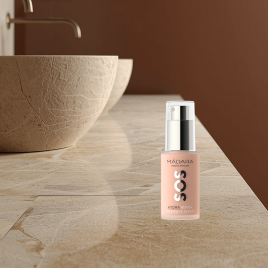Skincare serum bottle labeled 'SOS Hydra Repair Intensive Serum' by Mádara on a bathroom counter.