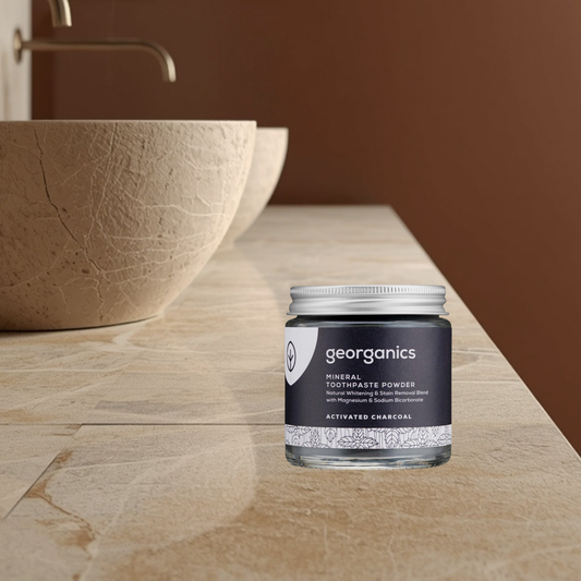 Georganics activated charcoal mineral toothpaste powder jar on a bathroom counter with a blurred background