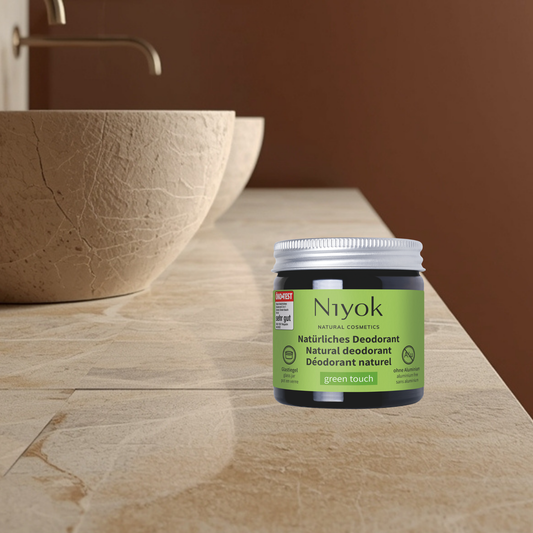 Niyok green touch natural deodorant jar on a bathroom counter with a brown bowl and sink in the background.
