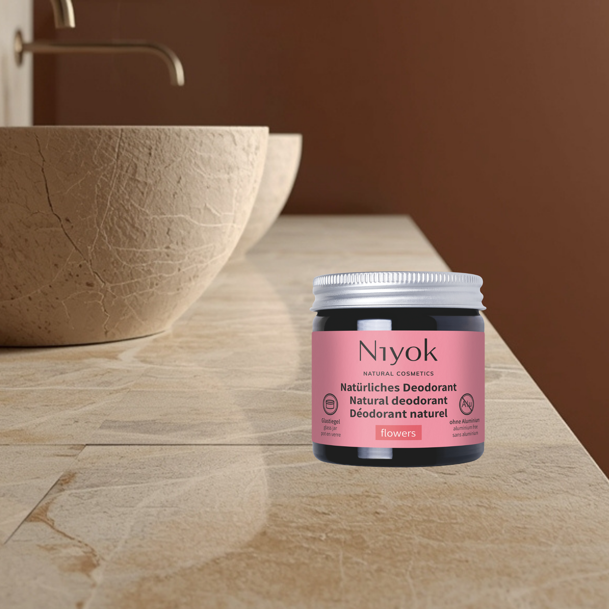 Niyok natural deodorant jar flowers on a bathroom counter with a brown bowl and sink in the background.