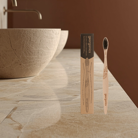 Georganics beechwood toothbrush and packaging on a bathroom counter with a brown background