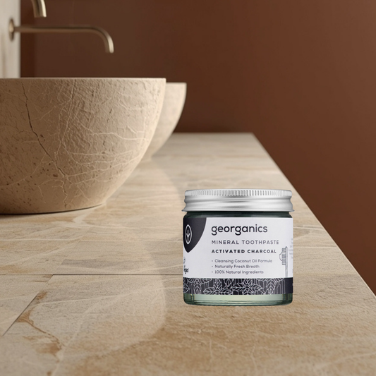 Georganics charcoal mineral toothpaste jar on a bathroom counter with a brown bowl and sink in the background.