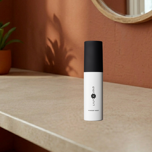 Makeup mist bottle with black cap on a beige surface against a brown wall.