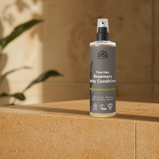Bottle of 'Fine Hair Rosemary Spray Conditioner' on a wooden surface with a plant in the background