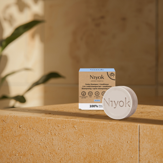 Niyok sensitive shampoo and conditioner bar and packaging on a stone surface with a blurred background