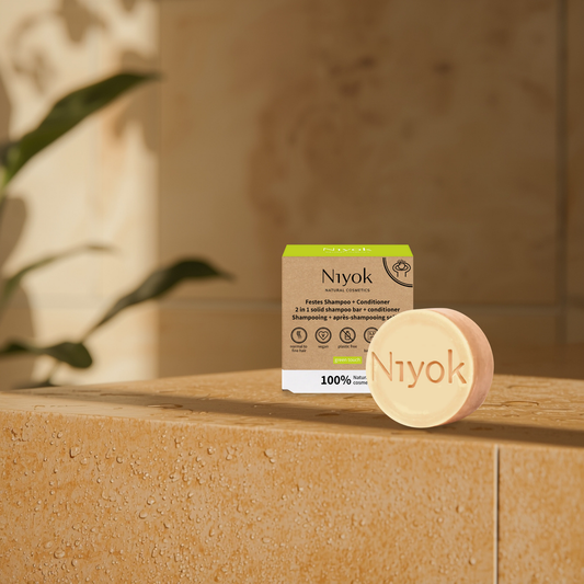 Niyok shampoo and conditioner bar and packaging on a stone surface with a blurred background