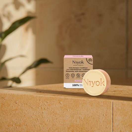 Niyok soft blossom shampoo and conditioner bar and packaging on a stone surface with a blurred background