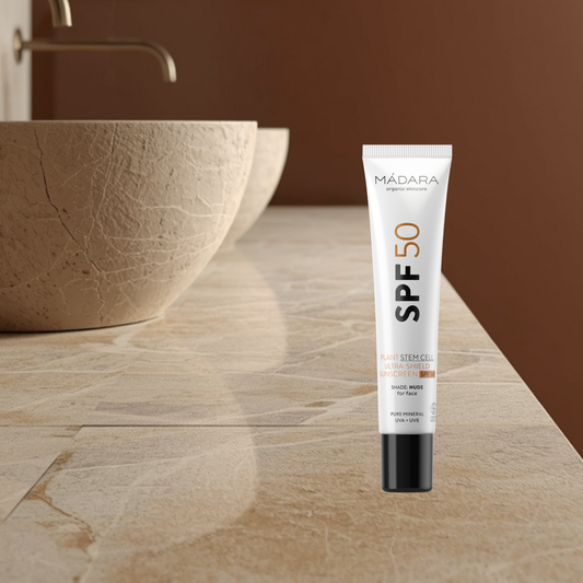 Mádara SPF 50 stem cell sunscreen tube on a bathroom counter with a brown bowl and faucet in the background.