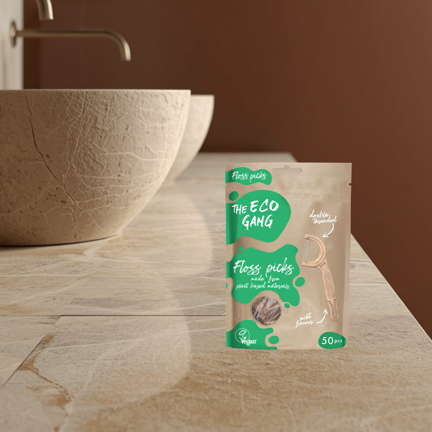 Packaging of 'The Eco Gang' floss picks on a bathroom counter with a brown bowl and sink in the background.