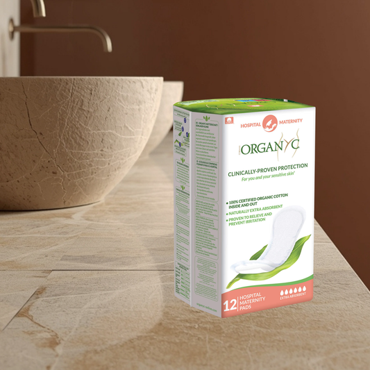 Box of Organyc hospital postpartum pads on a bathroom counter with a sink in the background.